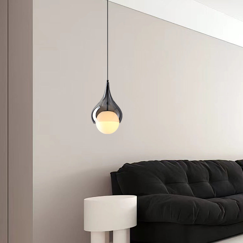 Een enkele hanglamp in de vorm van een waterdruppel boven een bank in een moderne kamer.