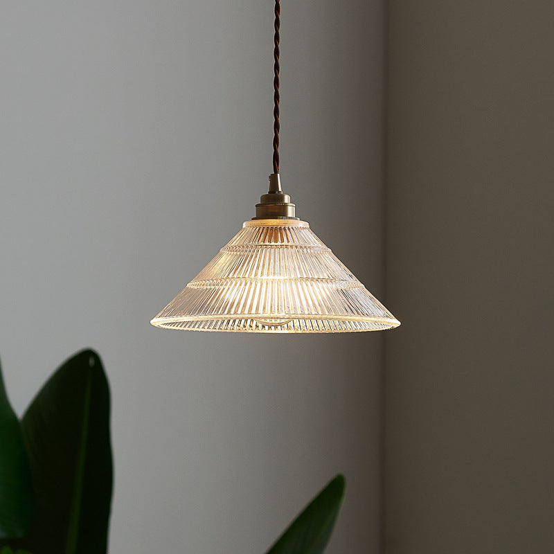 Eine beleuchtete, transparente Glaspendelleuchte in einem schlichten Raum mit Pflanzen
