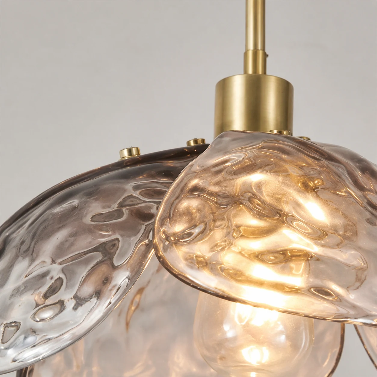 Vista ravvicinata del vetro martellato a forma di petalo e del connettore metallico della lampada a sospensione Flora.
